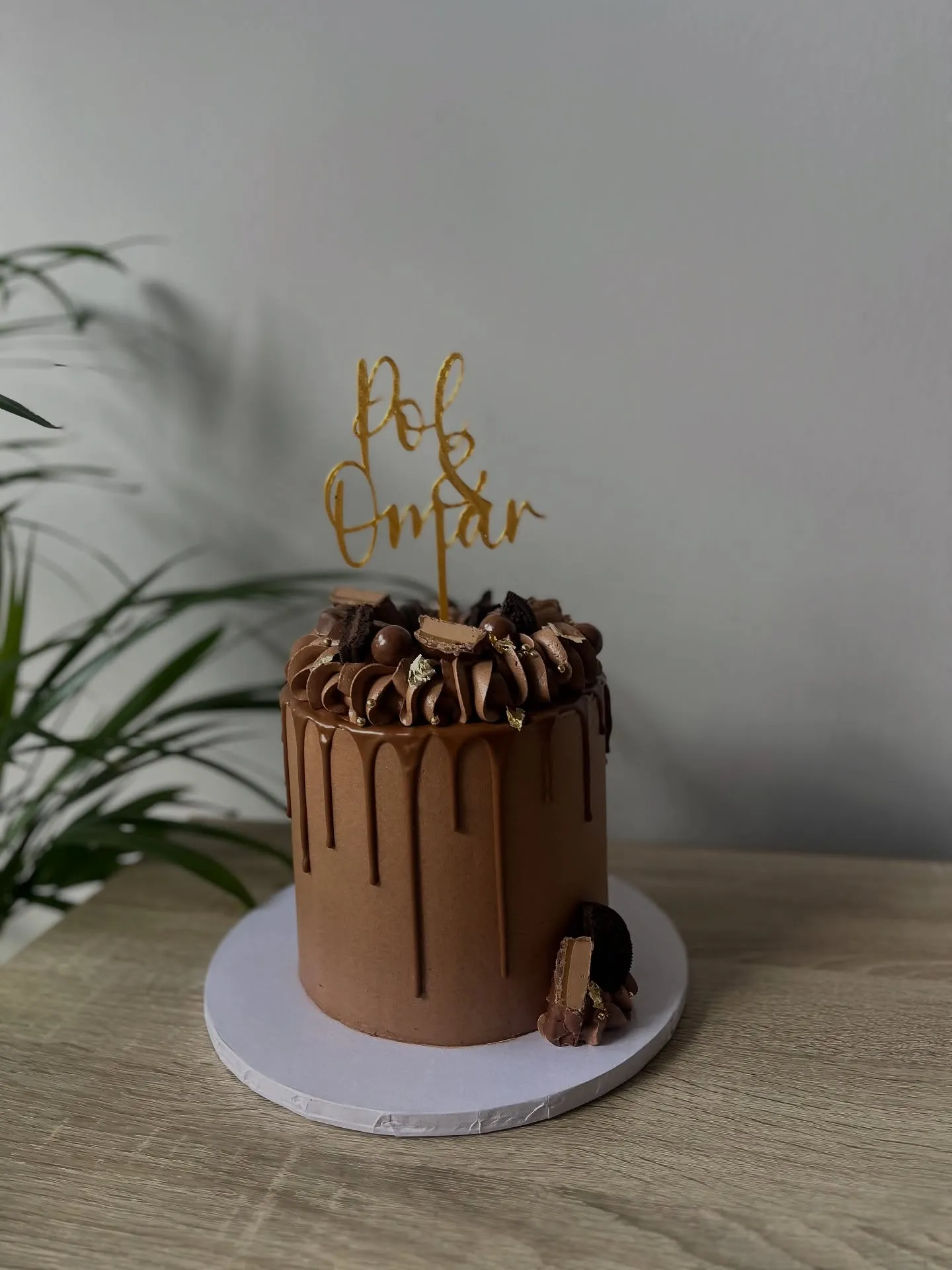 Chocolate drip cake topped with chocolates and a gold topper