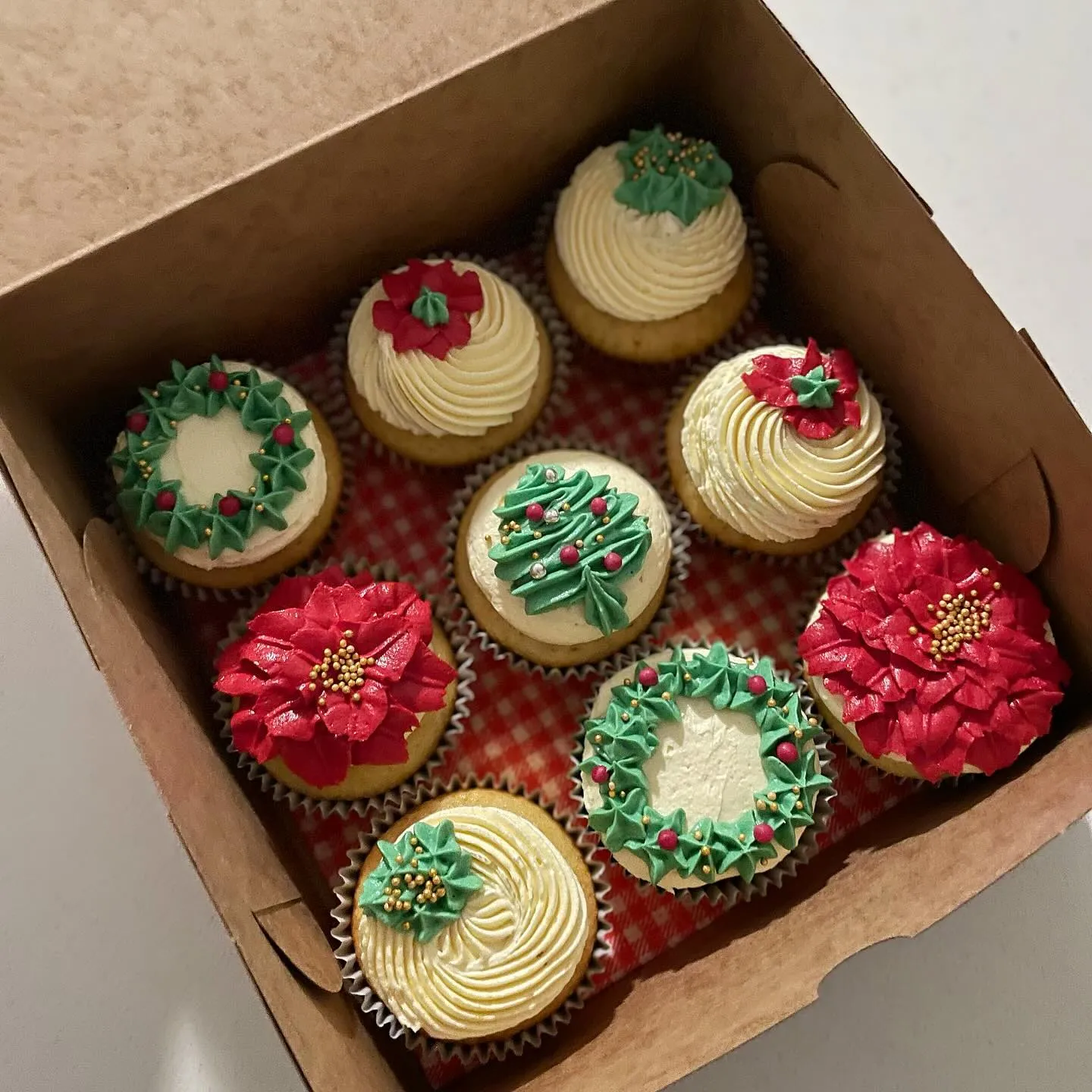 Box of festive cupcakes with poinsettia, wreath and tree piping