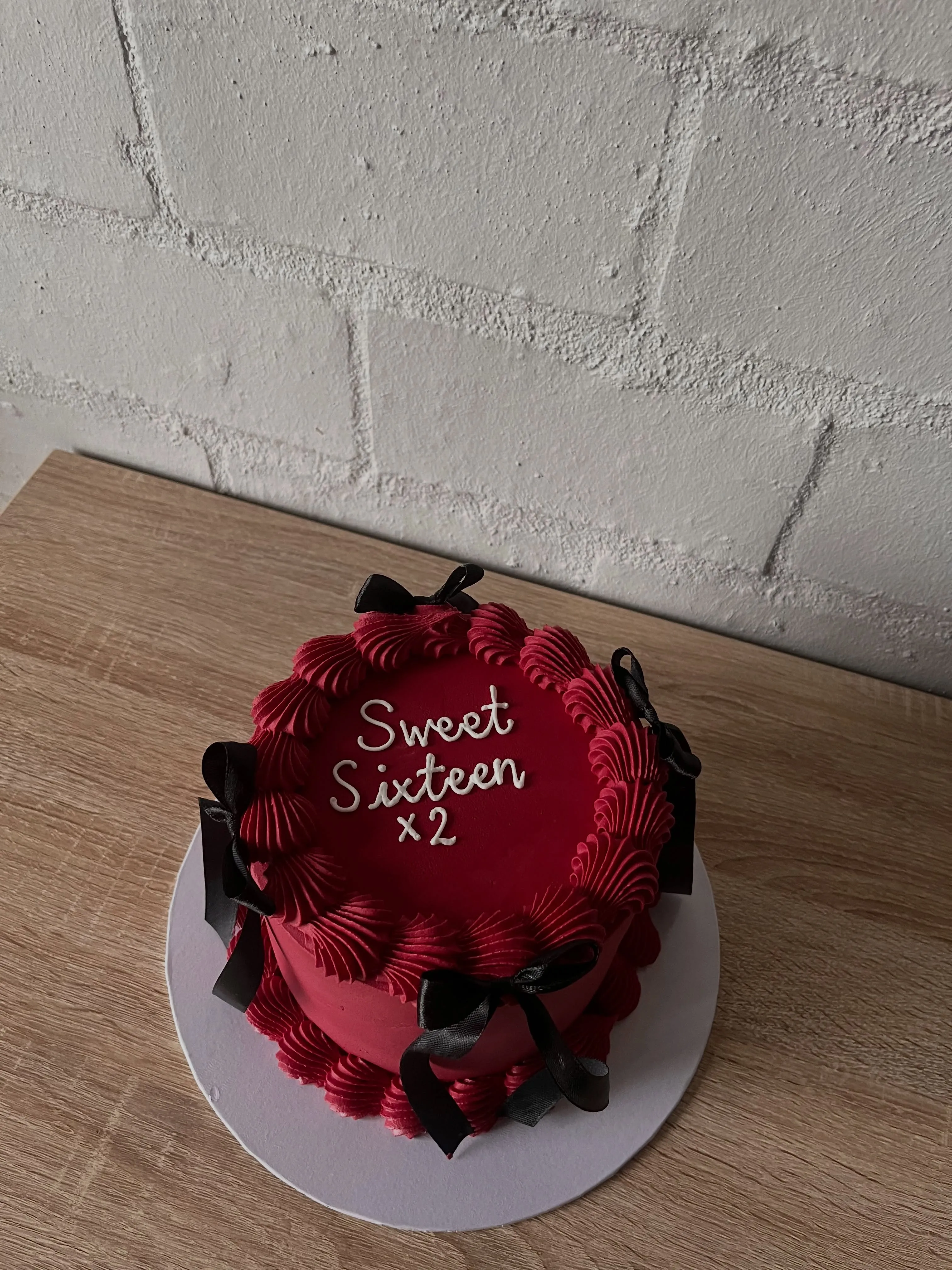 Cherry red cake piped with 'Sweet Sixteen x2', vintage buttercream shells and black satin bows