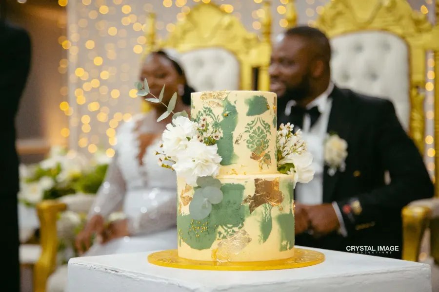 Two-tier sage and gold wedding cake with white flowers at a reception