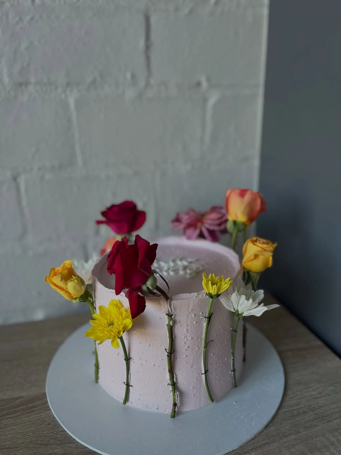 Pale pink cake wrapped with stemmed fresh roses and daisies